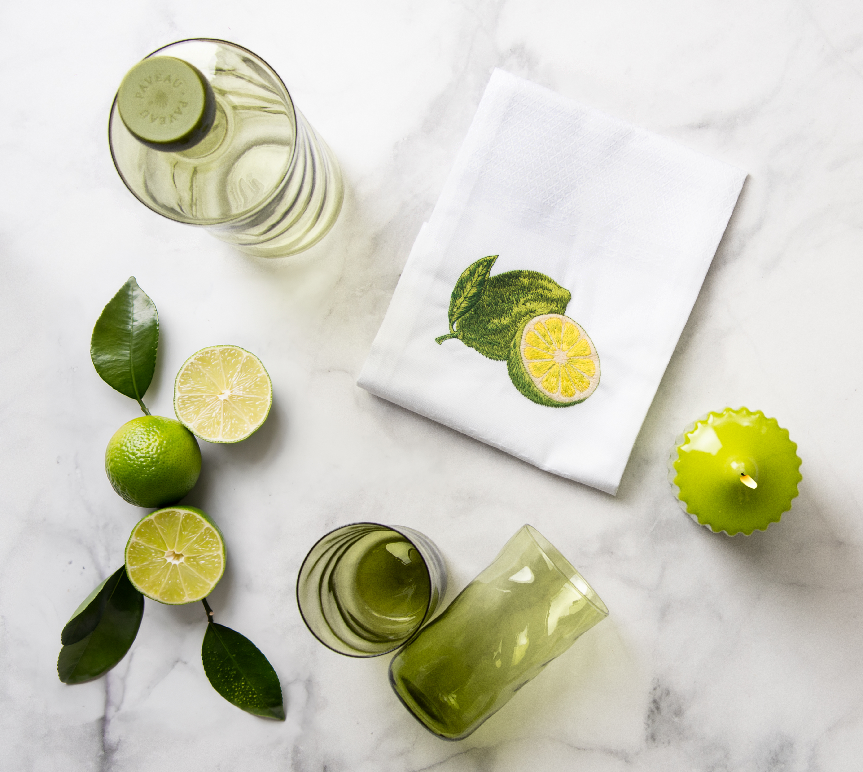 Ein gedeckter Marmortisch von oben fotografiert. Auf dem Tisch stehen grüne Tischaccessoieres sowie das Vista Portuguese Geschirrtuch mit dem Motiv Limette.