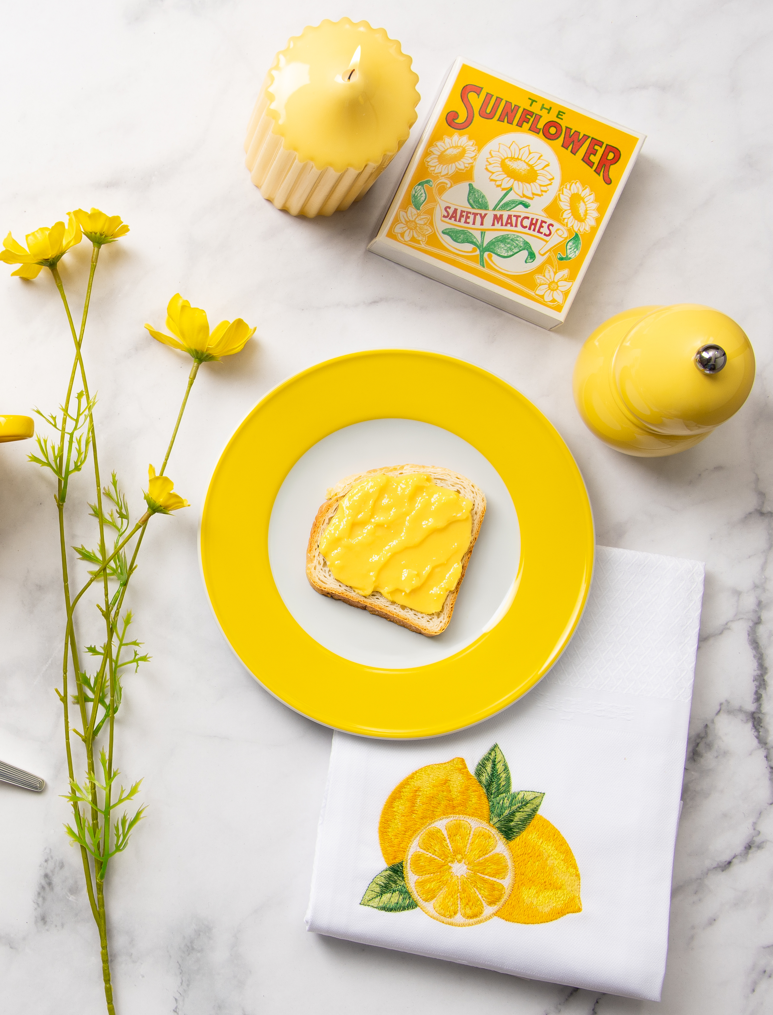 Ein gedeckter Marmortisch von oben fotografiert. Auf dem Tisch stehen vorwiegend gelbe Tischaccessoires sowie die gelbe Addison Ross Salz- und Pfeffermühle.