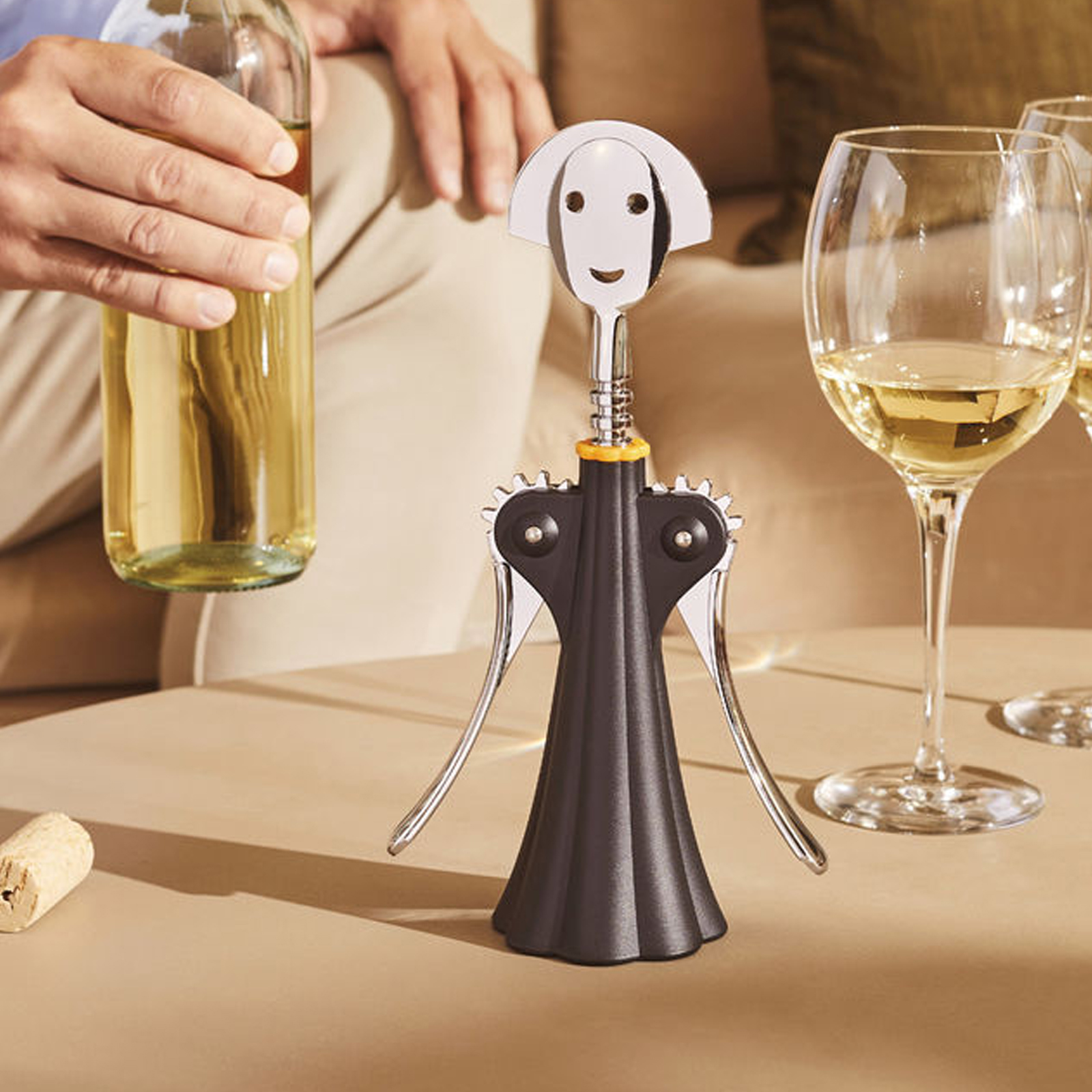 Der Alessi Korkenzieher Anna G. in schwarz auf einem gedeckten Wohnzimmertisch, auf den gerade eine Weinflasche gestellt wird.