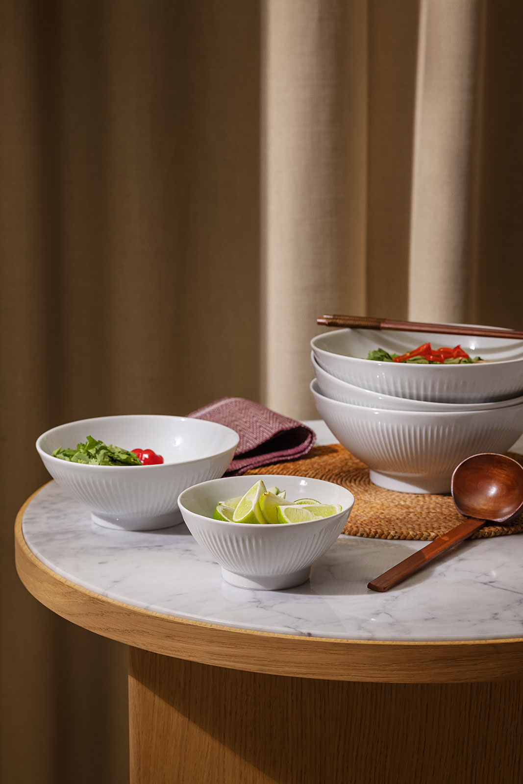 Auf einem runden Tisch ist alles angerichtet, um leckere Ramen-Nudeln zu genießen. In kleineren Schalen sind Gemüse und Zitronenschlitze, um das Gericht zu ergänzen.