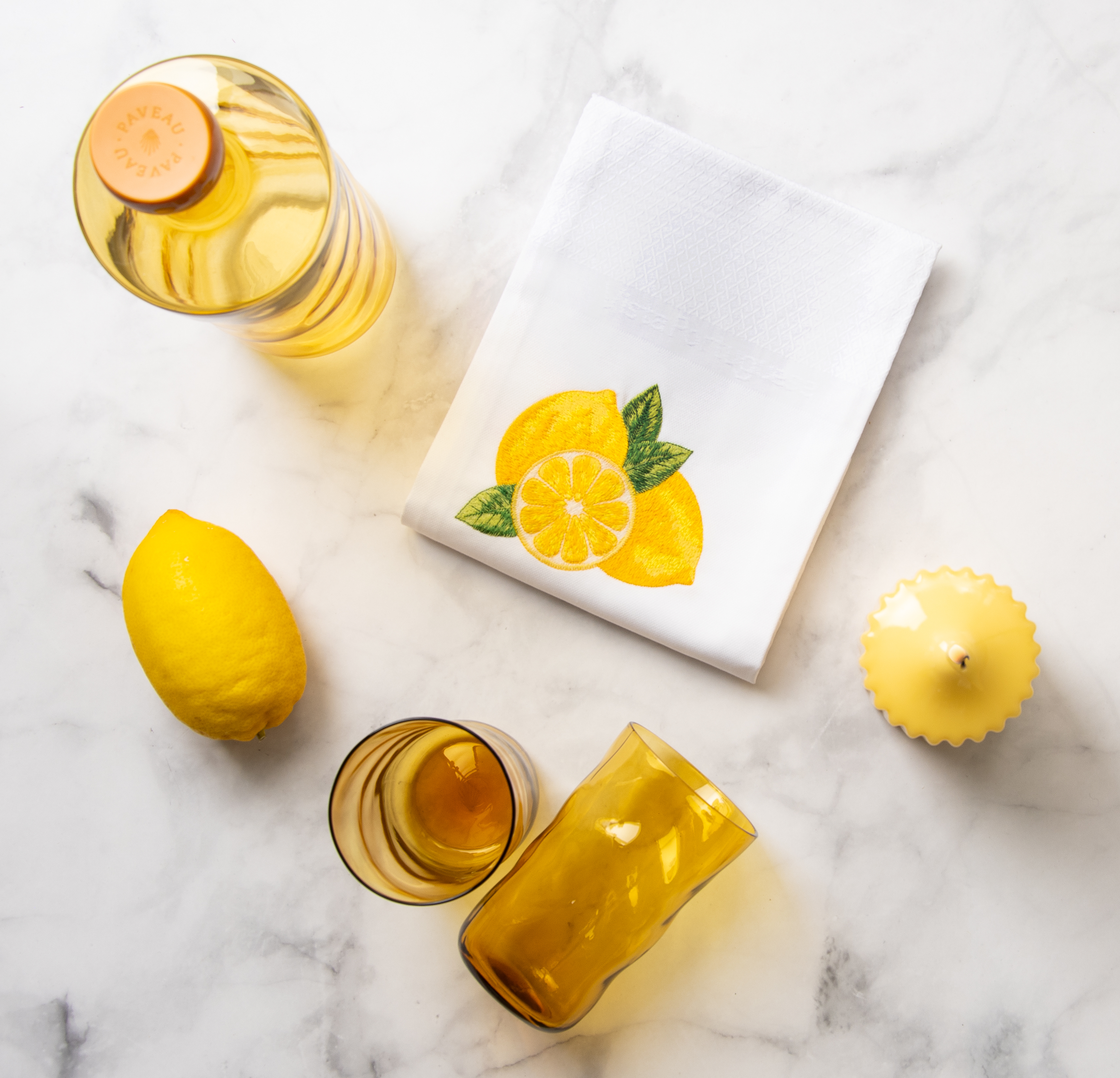 Ein gedeckter Marmortisch von oben fotografiert. Auf dem Tisch stehen gelbe Tischaccessoieres sowie das Vista Portuguese Geschirrtuch mit dem Motiv Zitrone.