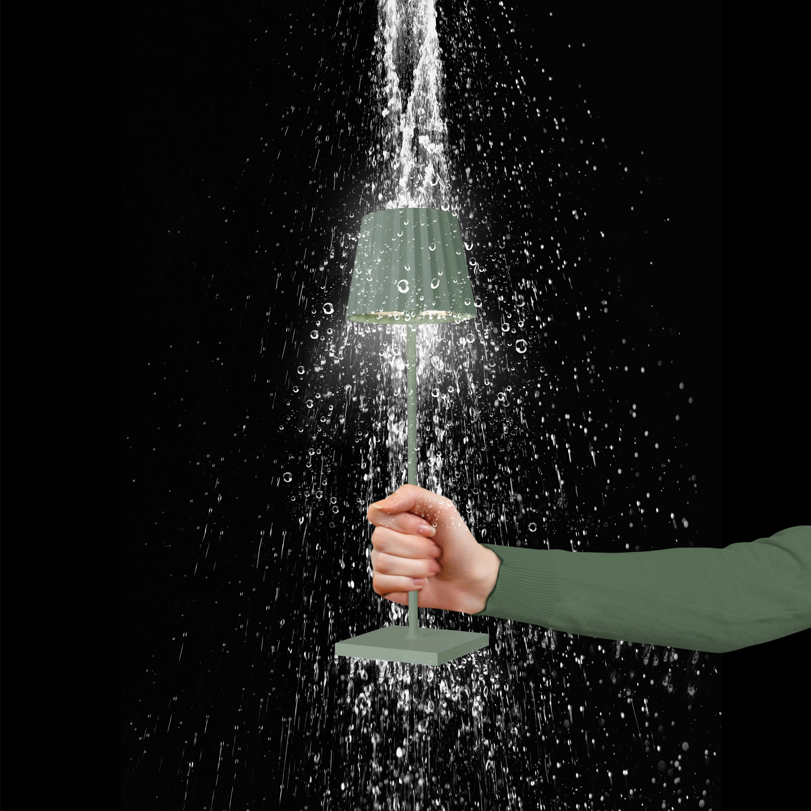 Eine weibliche Hand, die eine olivgrüne Akku-Tischleuchte in den Regen hält.