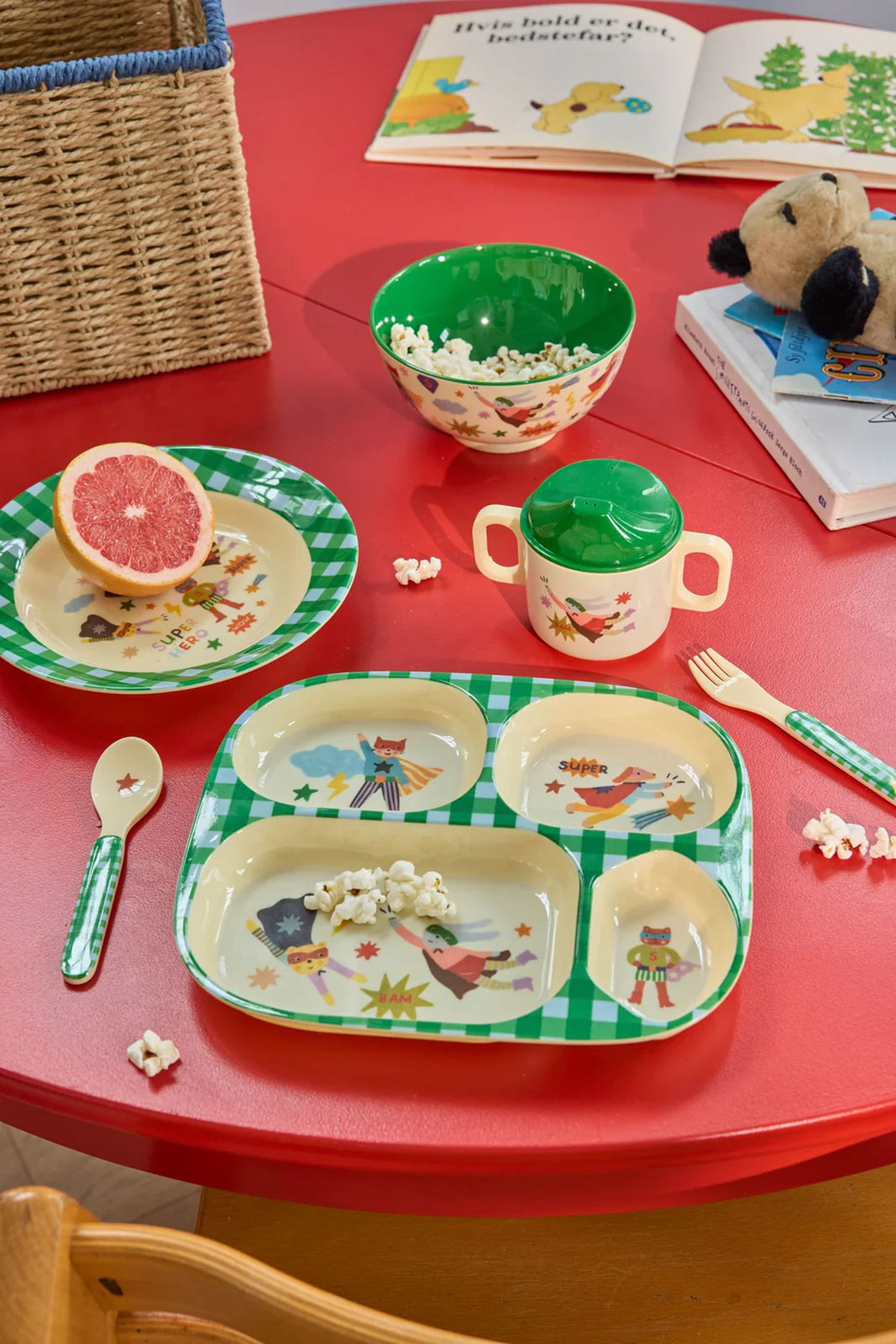 Auf einem roten Tisch ist das Frühstück serviert auf dem Hero Print Kindergeschirr in Grün.