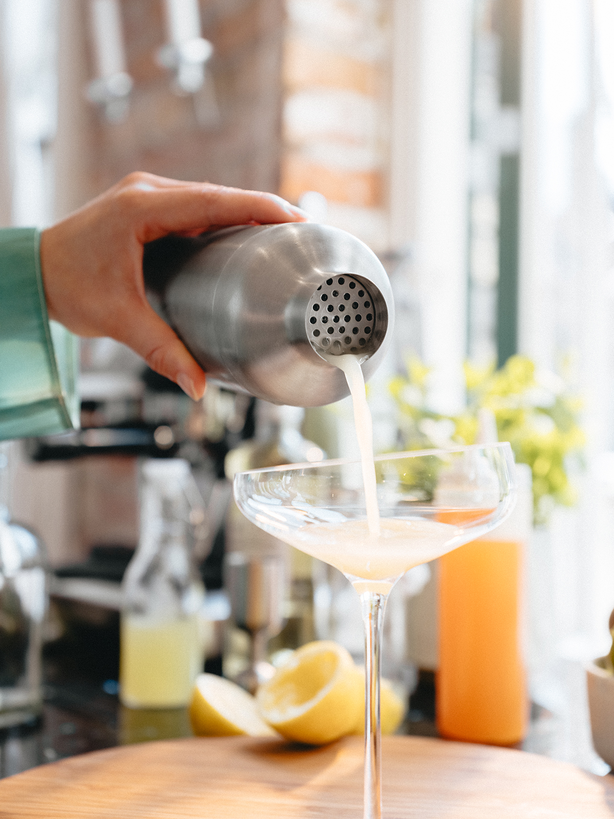 Nahaufnahme eines Cocktailglases in das, mithilfe des Shakers, gerade ein Cocktail gegossen wird.