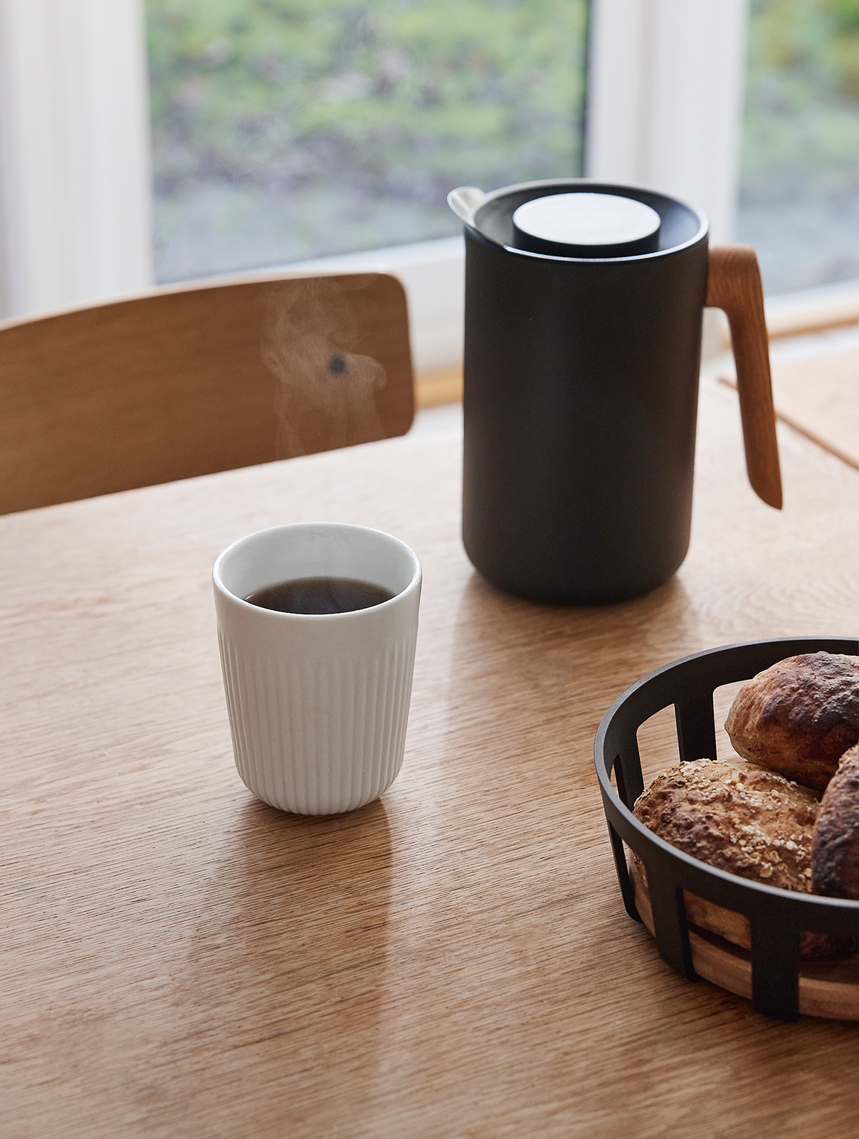 Ein Esstisch mit der Nordic Kitchen Isolierkanne, einem Brotkorm und einem Kaffeebecher.