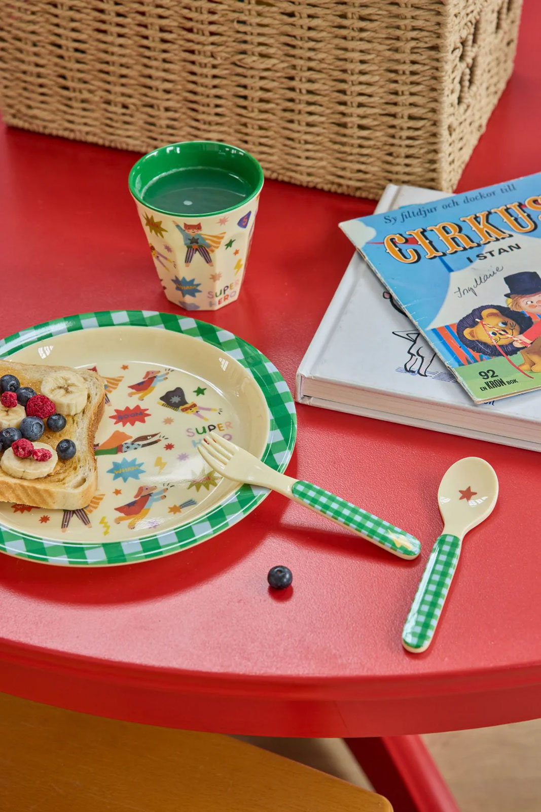 Auf einem pinken Tisch isst jemand gerade von seinem Hero Print Kinderteller grün sein Frühstück.