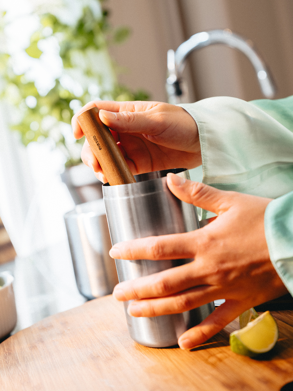Nahaufnahme, wie auf einer Küchenzeile der Cocktail-Stößel verwendet wird. Der Stößel wird von einer weiblichen Hand gehalten und im Cocktailshaker zum Einsatz gebracht.