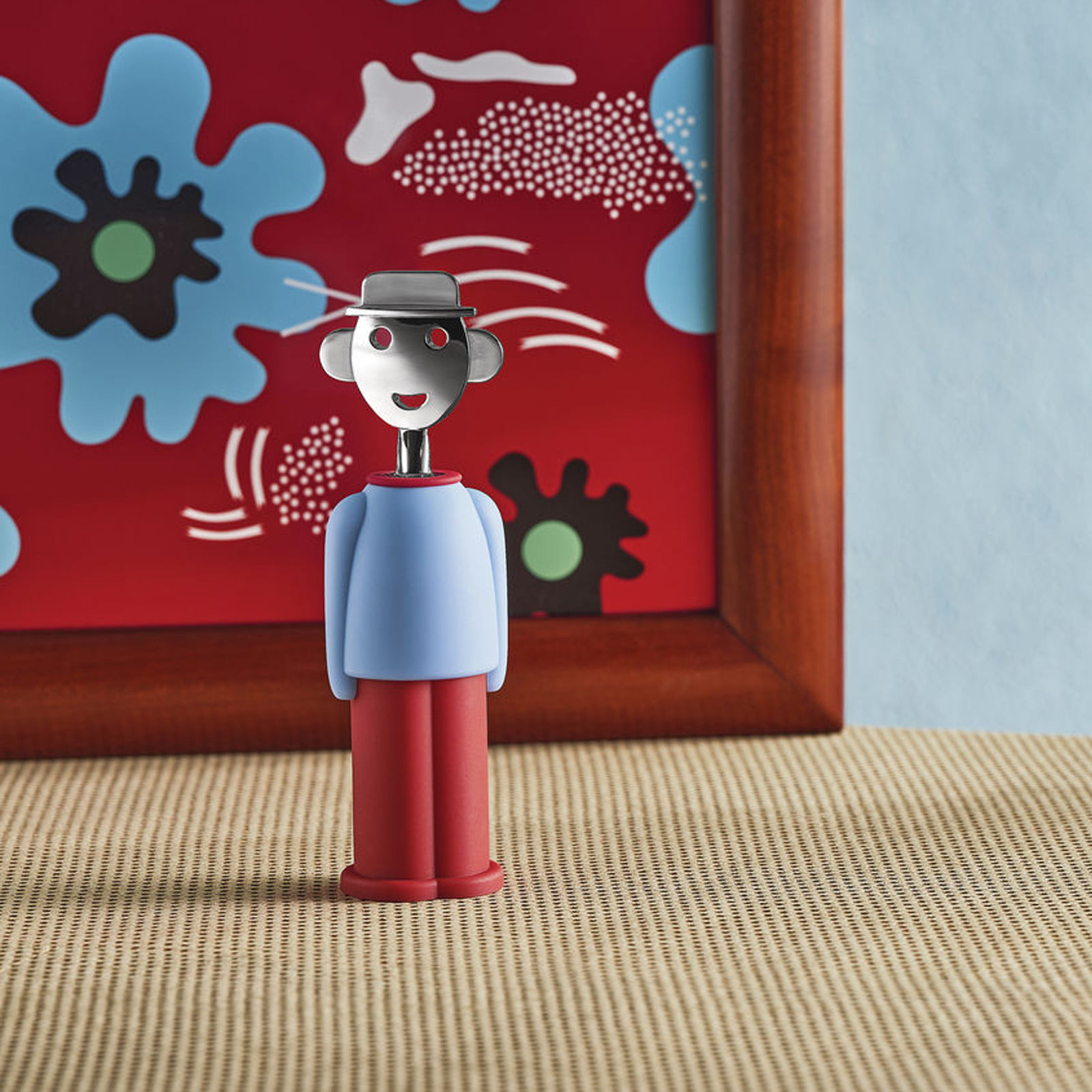 Alessi Alessandro M. Korkenzieher in hellblau-rot von Alessandro Mendini auf einem gedeckten Tisch.