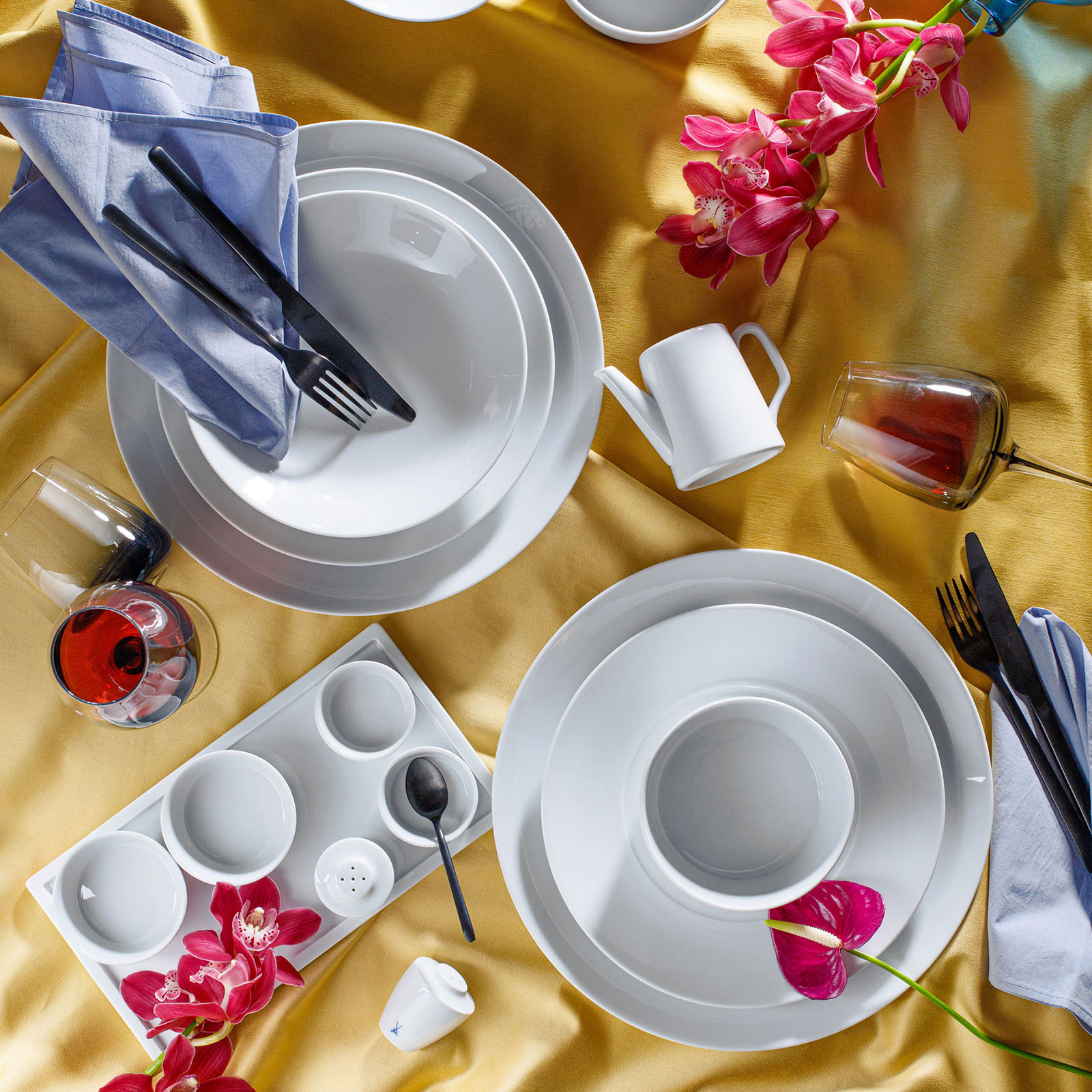 Auf einer gelben Tischdecke ist eingedeckt mit dem edlen Cosmopolitan weiß Geschirr von Meissen. Der Tisch ist dekoriert mit pinken Orchideen.