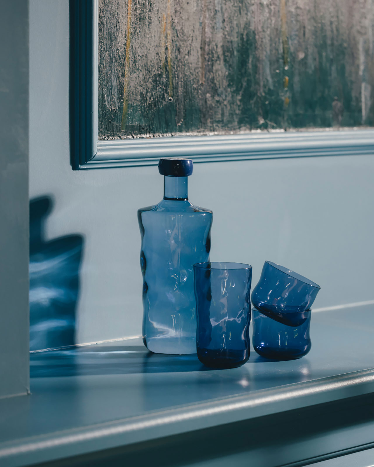 Eine Wasserflasche aus dunkelblauem Glas steht neben ineinandergestapelten Trinkgläsern der gleichen Farbe.