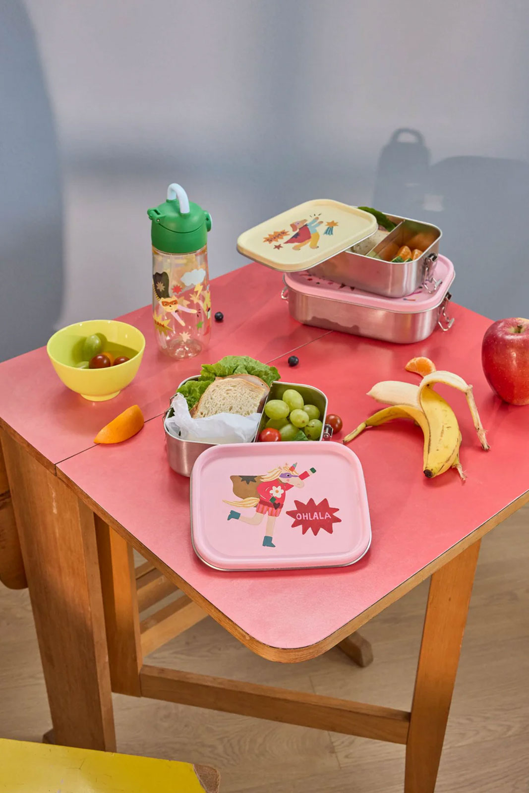 Auf einem pinken Tisch sind einige Hero Print Brotdosen für ein Picknick angerichtet.