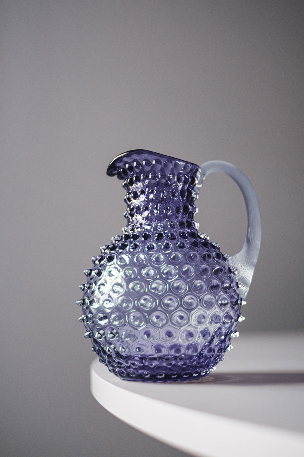 Der Paris Hobnail Krug Indigo steht vor grauem Hintergrund auf einem Tisch.