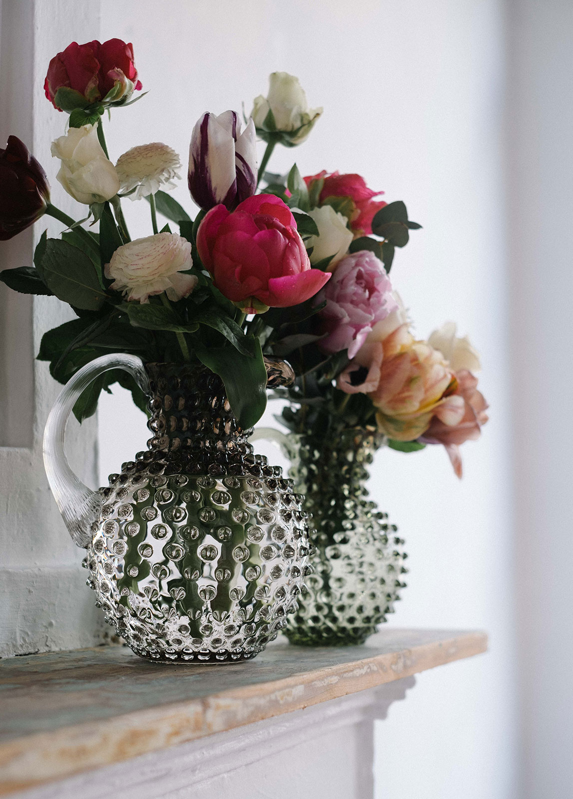Auf einem mamornen Kaminsims steht der Paris Hobnail Krug Crystal von Anna von Lipa umfunktioniert als Blumenvase für hübsche Pfingstrosen.