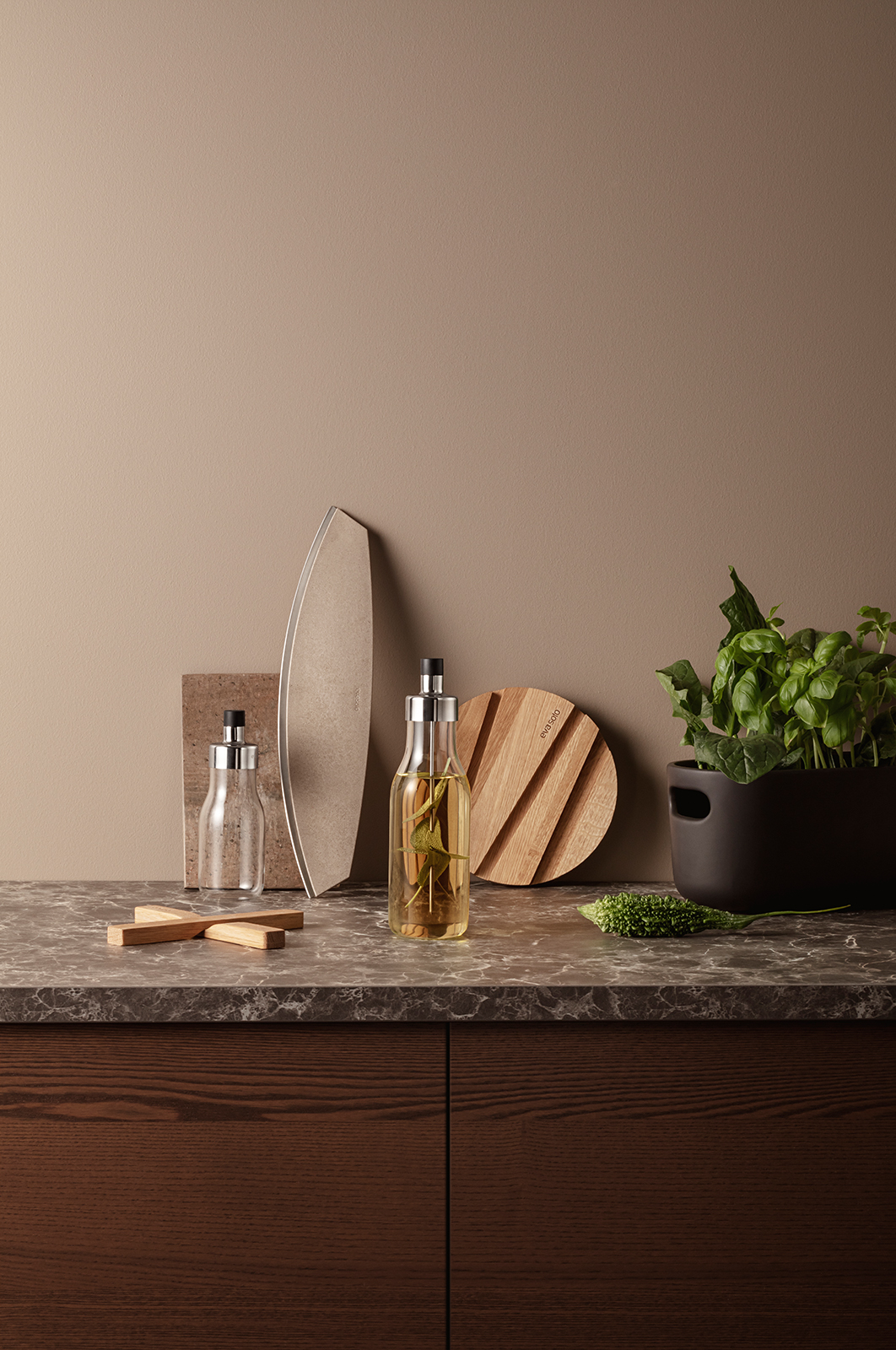 Eine Küchenarbeitsplatte vor einer beigen Wand. Auf der Platte befinden sich zwei My Flavour Karaffen - eine große und eine kleine. Im Hintergrund sind Schneidebretter und Kräuter.