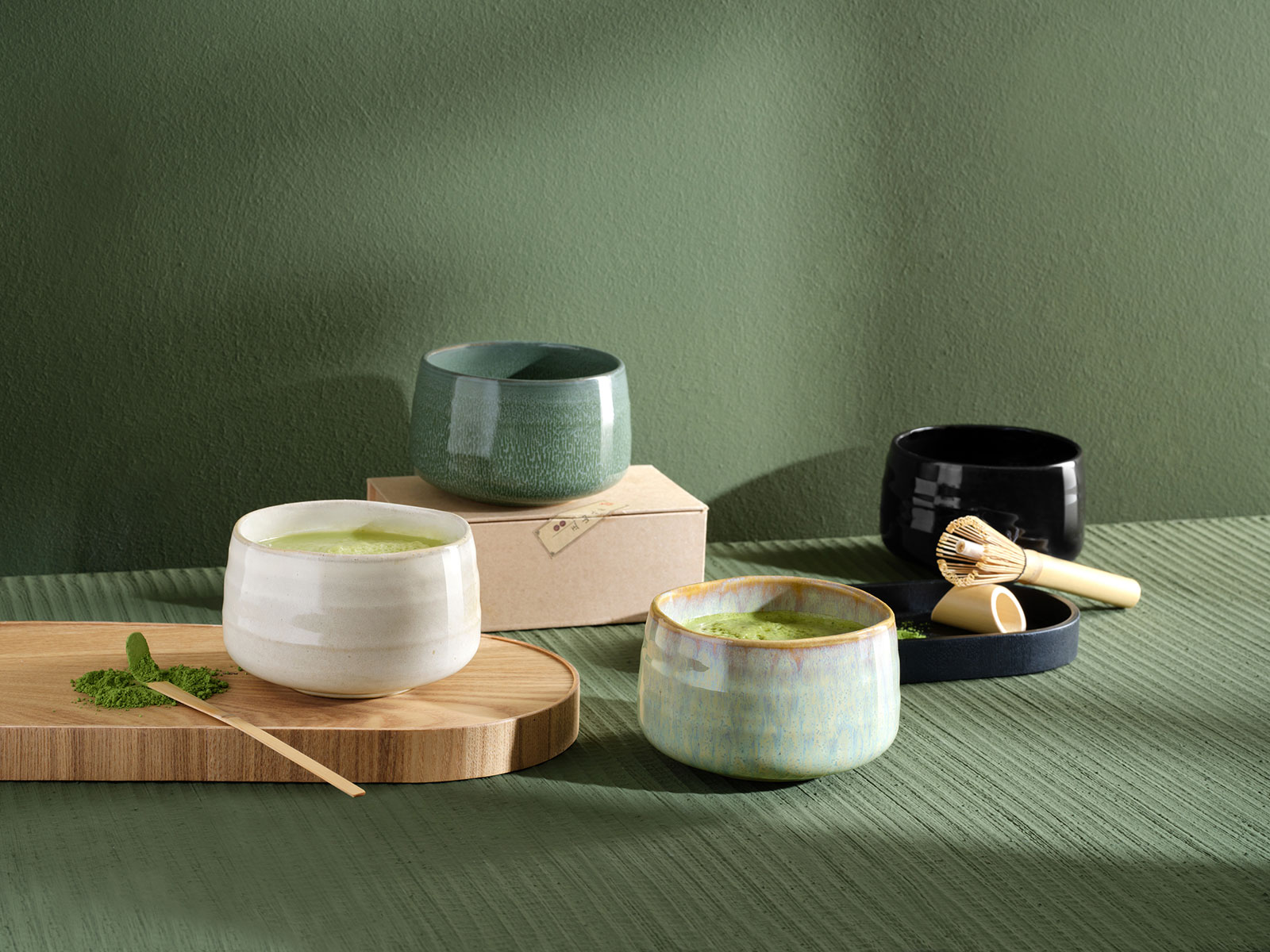 Vor einem grünen Hintergrund stehen vier Moribana Matcha Schalen verschiedener Farben.