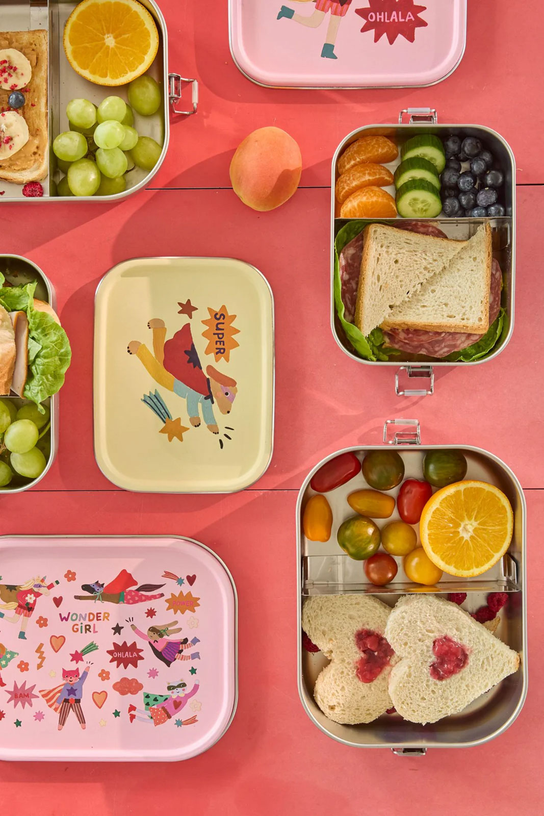 Draufsicht auf einen pinken Tisch, auf dem Hero Print Brotdosen mit liebevol hergerichteten herzförmigen Pausenbroten stehen.