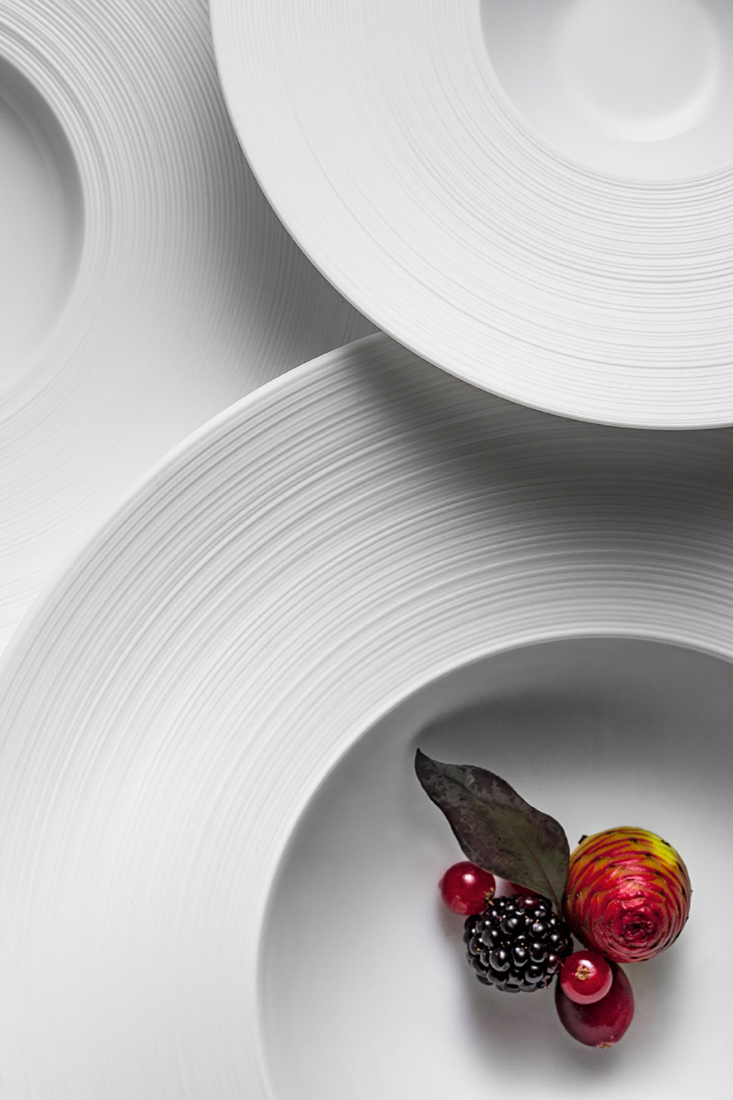 Detailansicht von oben. Rote Früchte liegen im Hémisphère Satin white Suppenteller von Coquet. Das Schattenspiel zeigt, wie eden das Rillen-Finish auf der Fahne aussieht.