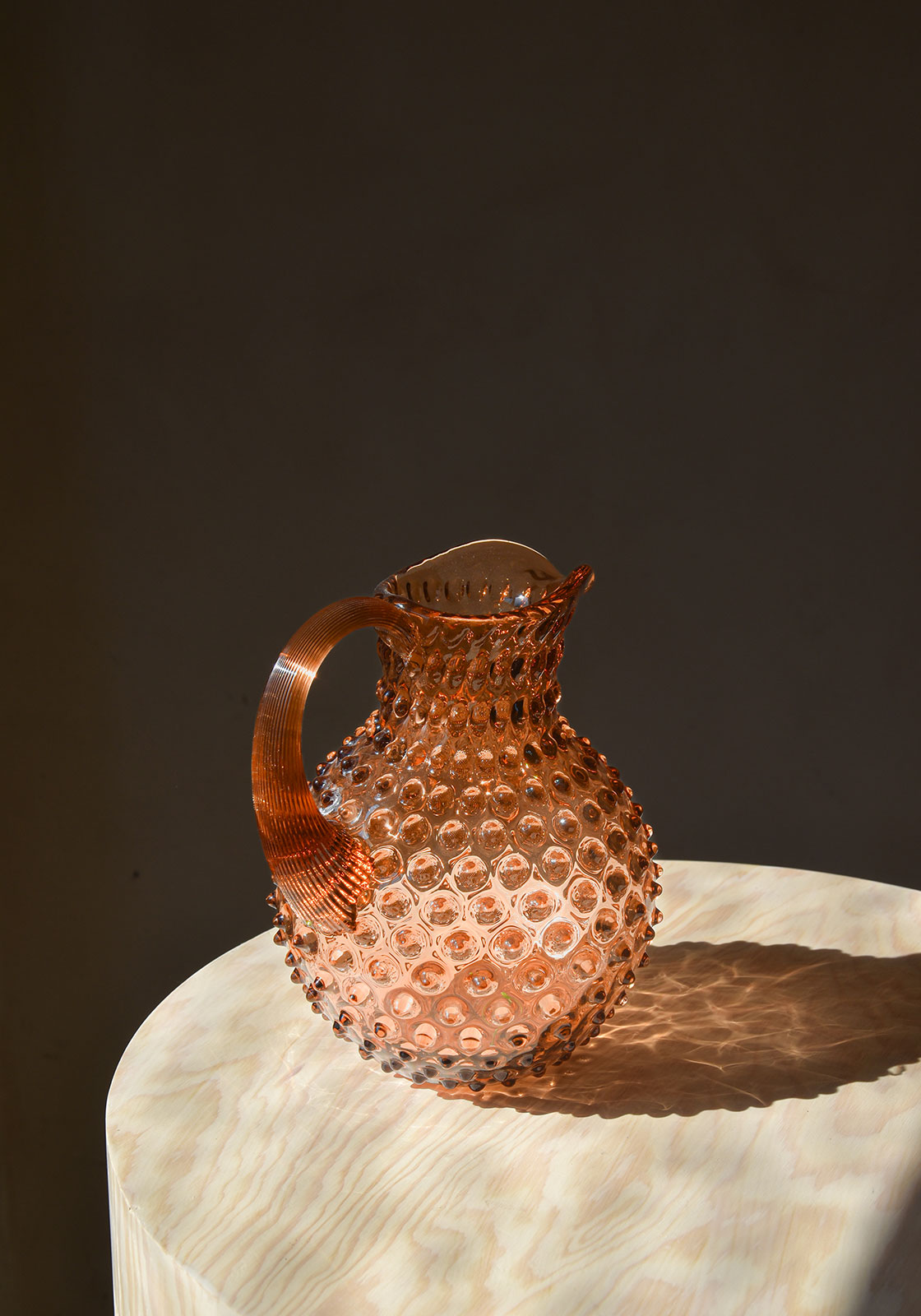 Ein Sonnenstrahl trifft den Paris Hobnail Krug in New Brown, der auf einem Mamortisch steht.