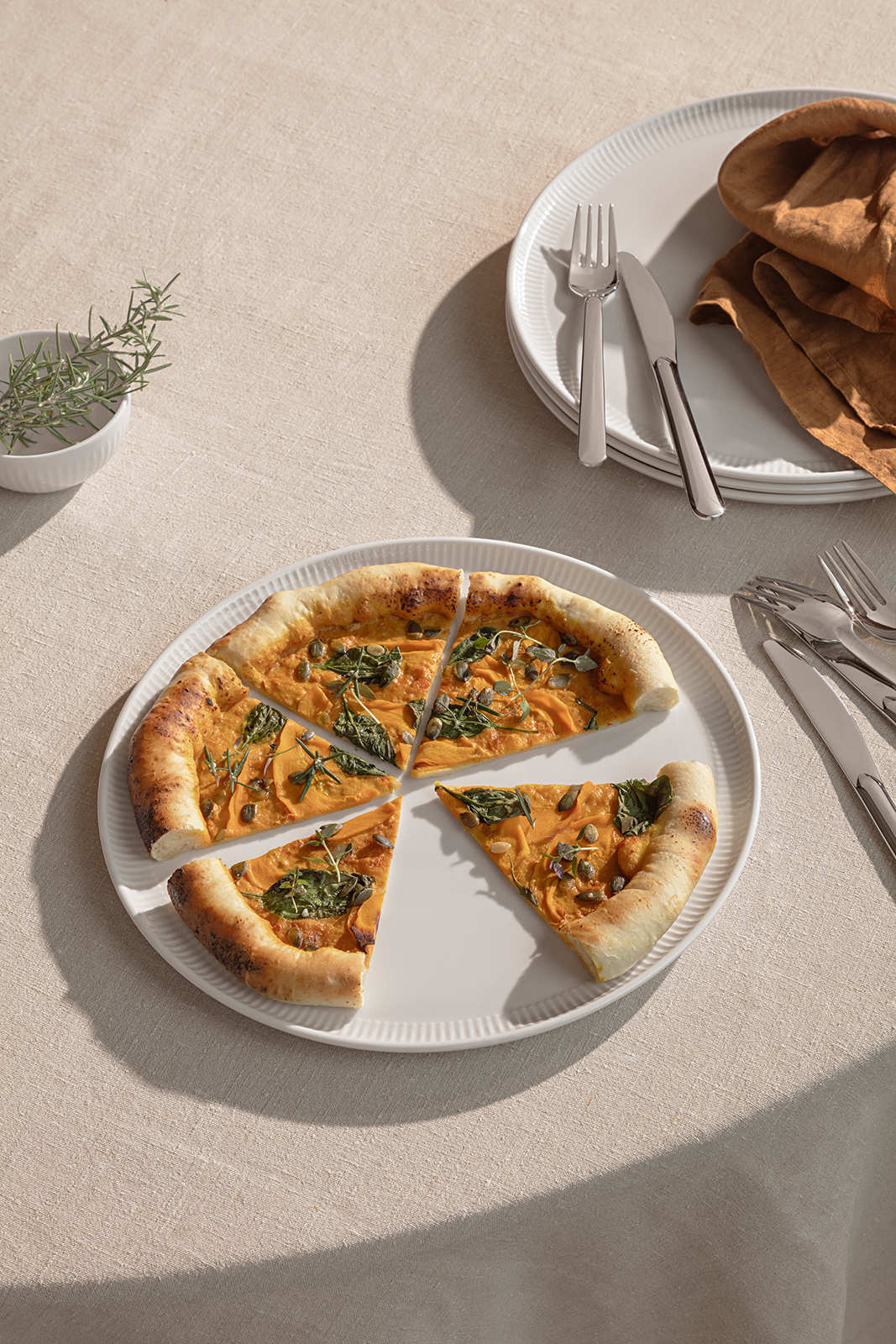 Ein gedeckter Tisch mit Geschirr - im Vordergrund der Pizzateller mit einer Pizza.