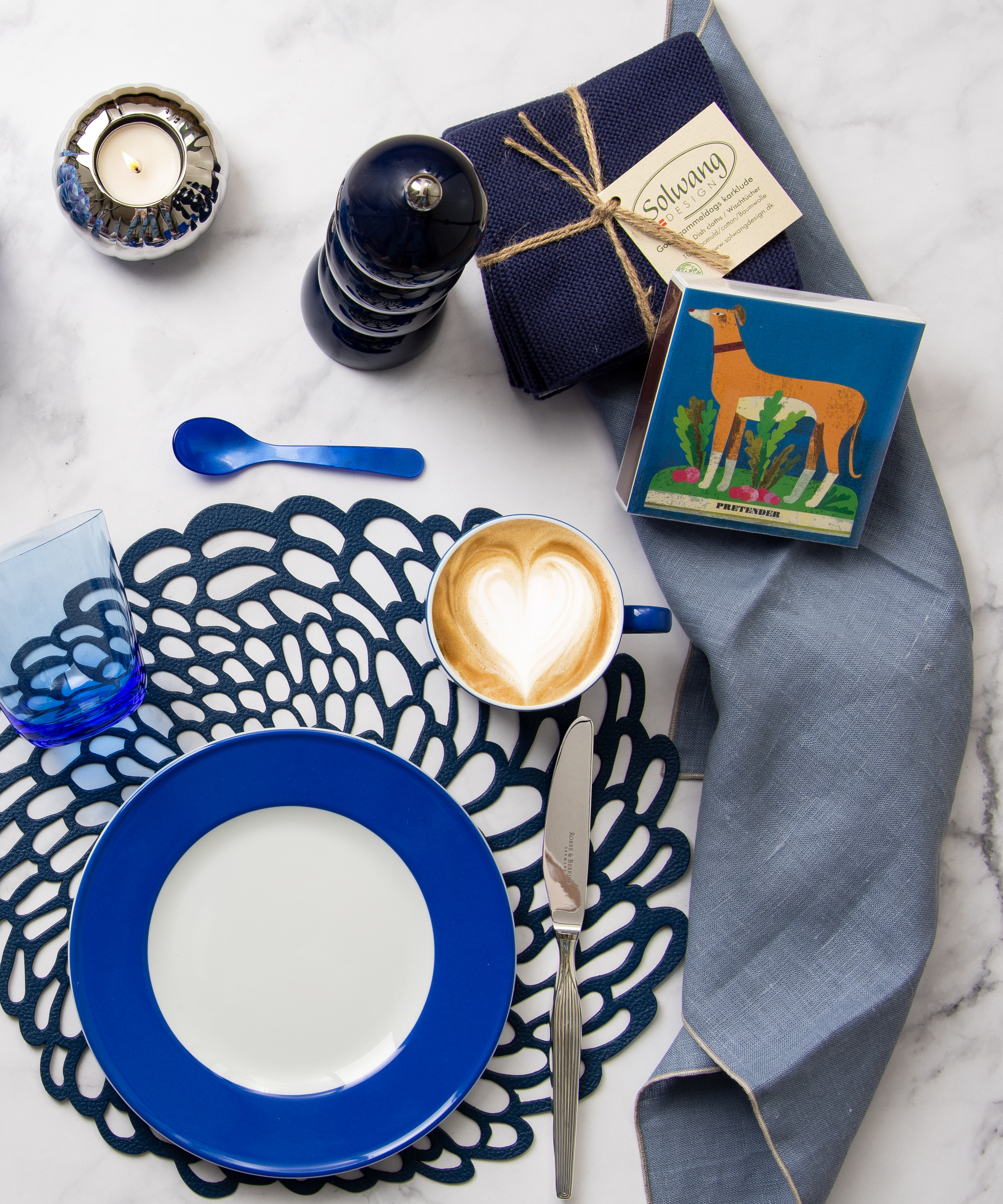 Ein gedeckter Marmortisch von oben fotografiert. Auf dem Tisch stehen vorwiegend blaue Tischaccessoires sowie eine taubenblaue Leinen-Serviette von Erika Vaitkute.
