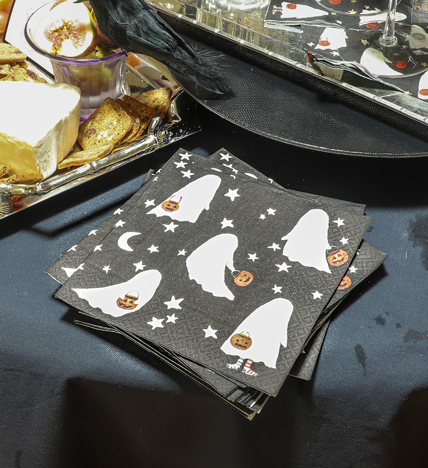Ein Halloween dekorierter Tisch, in dessen Mittelpunkt die Caspari Servietten mit Geister-Motiv liegen. Die weißen Gespenster sind mit Sternen auf einer schwarzen Serviette abgebildet.