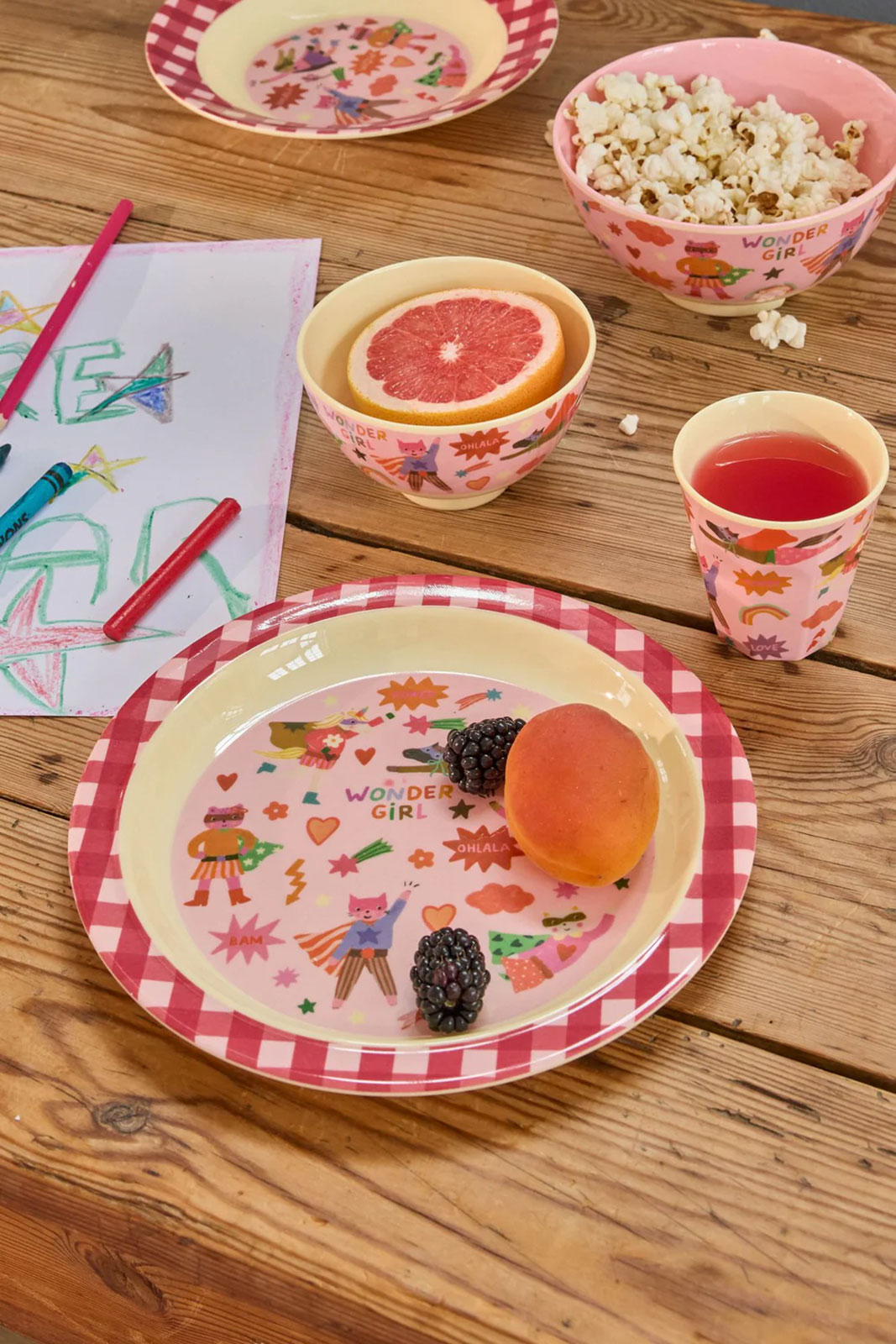 Auf einem Holztisch wird jemandem gerade auf dem Hero Print Kinderteller pink sein Frühstück serviert.