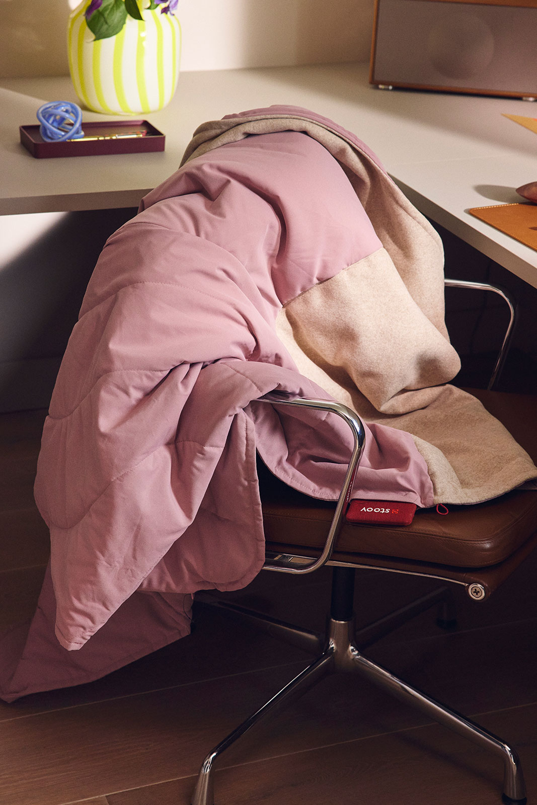 Die Huge Hug Heizdecke Original Soft Pink liegt zusammengebündelt auf einem Schreibtischstuhl.